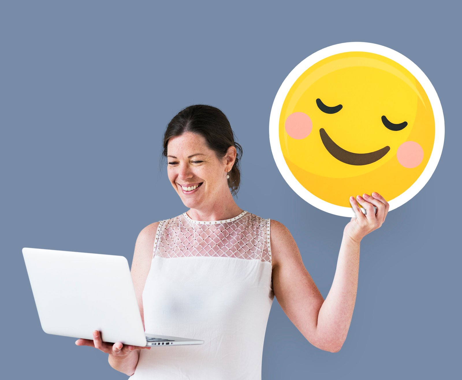 woman holding blushing emoticon using laptop scaled